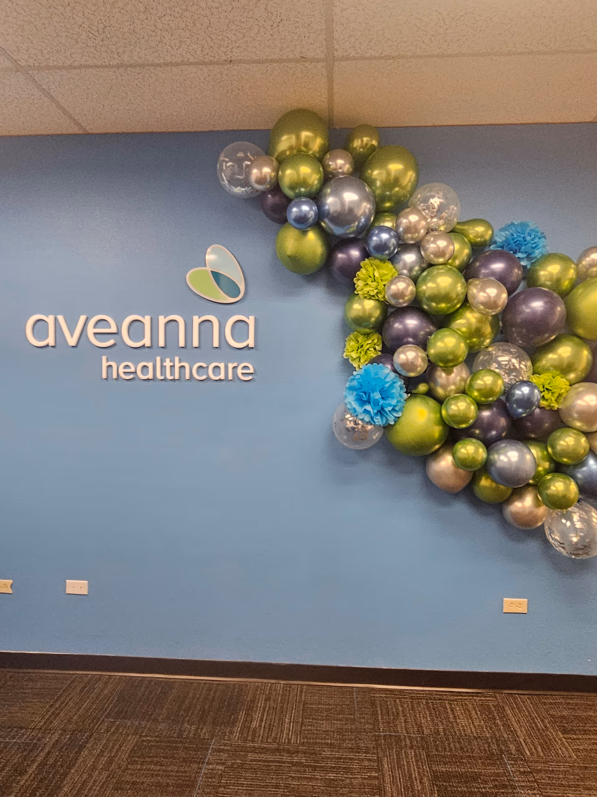 Blue wall with Aveanna Healthcare logo and colorful balloon arrangement in a lobby.