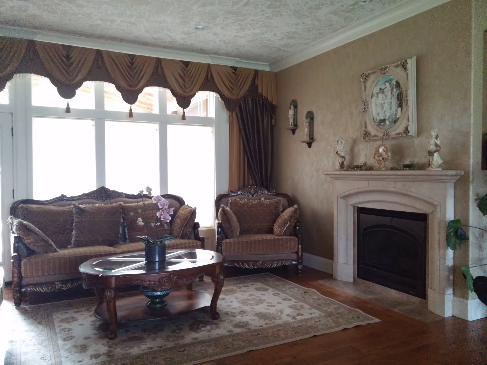 Elegant living room with ornate sofa set, fireplace, and large arched windows.