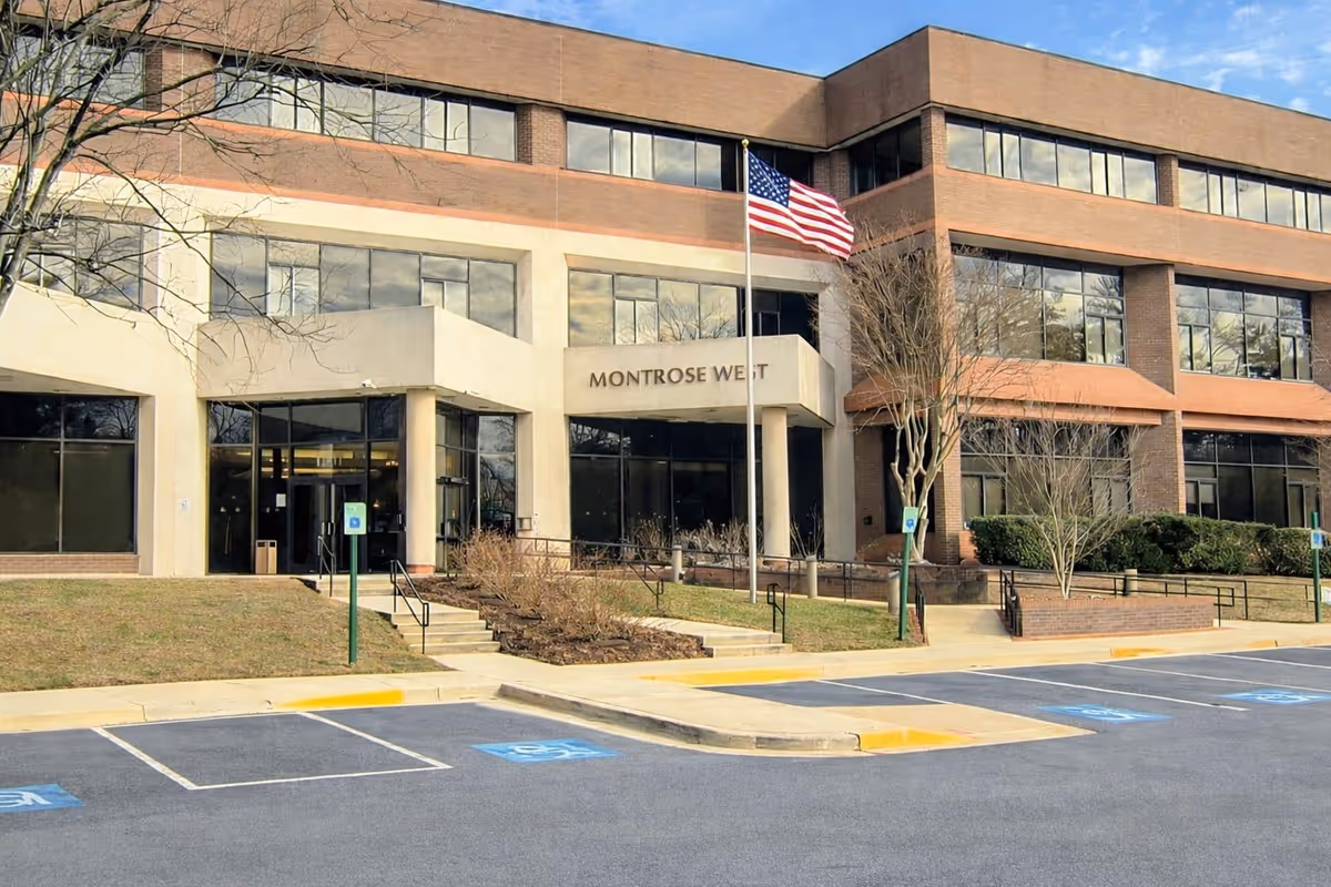 Exterior view of a two-story senior living facility with flagpole and parking lot.