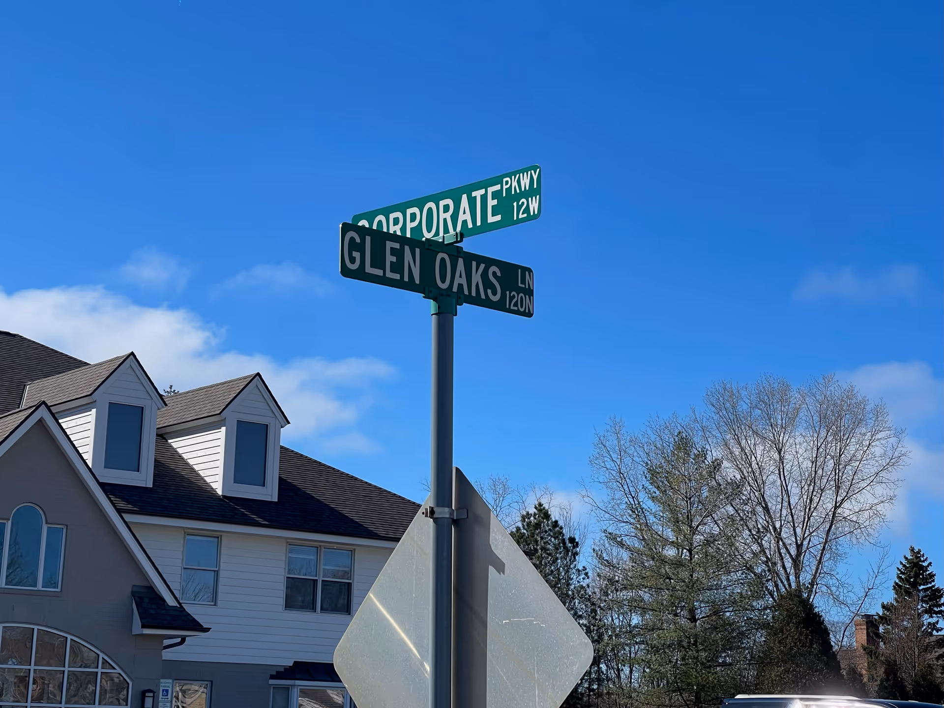 Street signs at a corner beside a two-story residential-style building against blue sky.