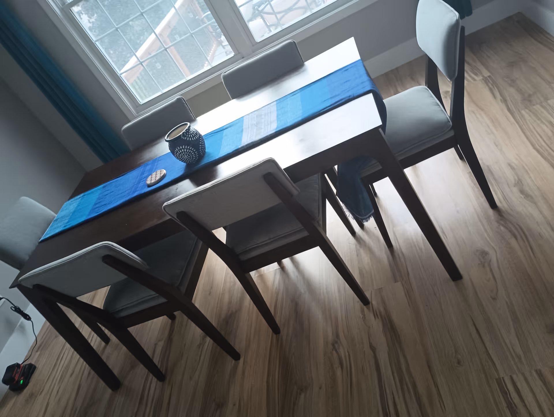 Wood dining table with blue runners and six chairs in a bright dining area.