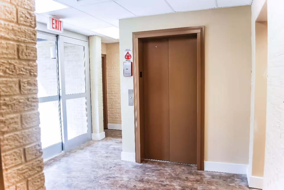 Interior hallway with brown elevator doors, glass exit door, and beige brick walls.