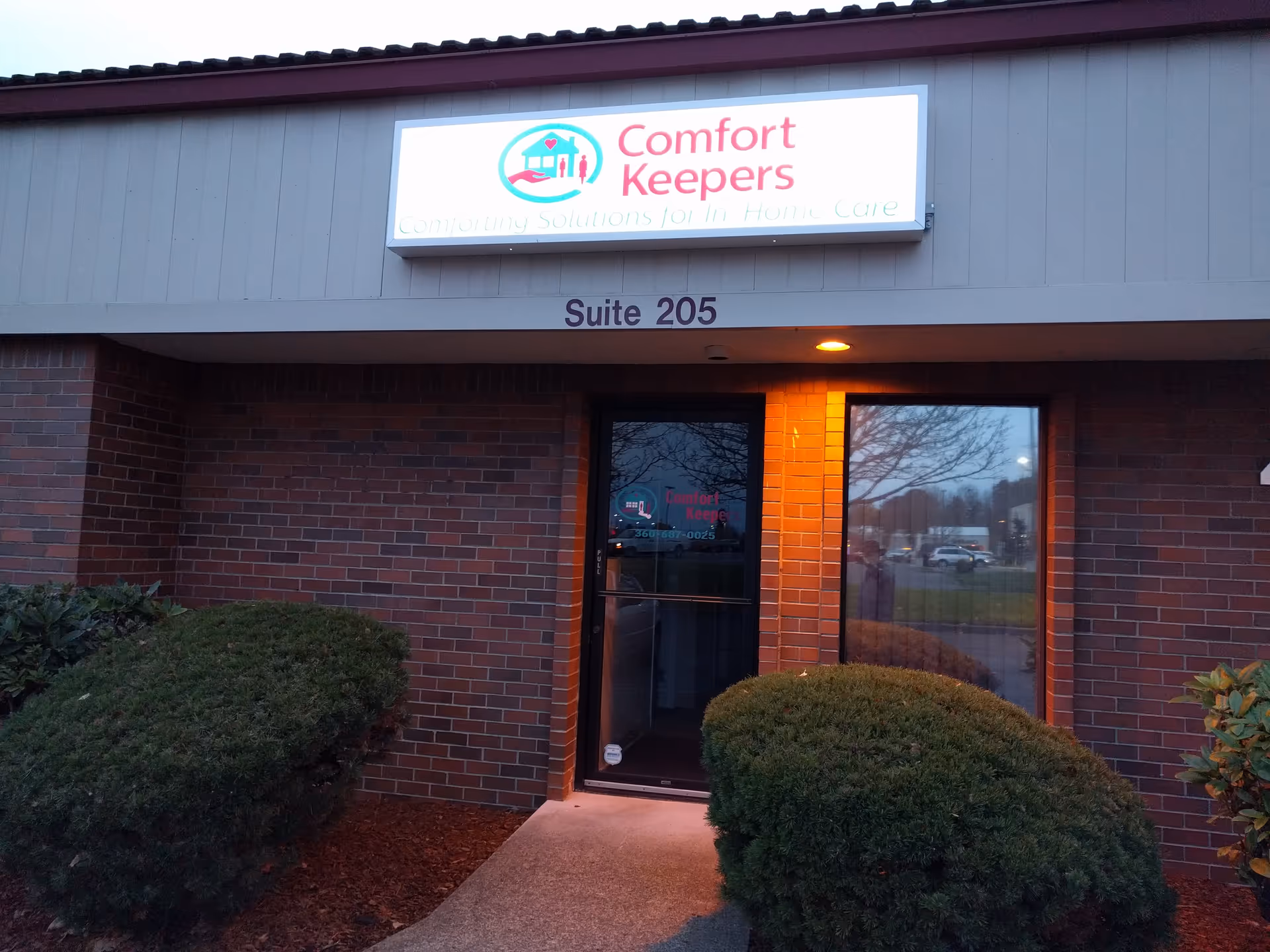 Exterior view of Comfort Keepers building entrance with sign and trimmed shrubs