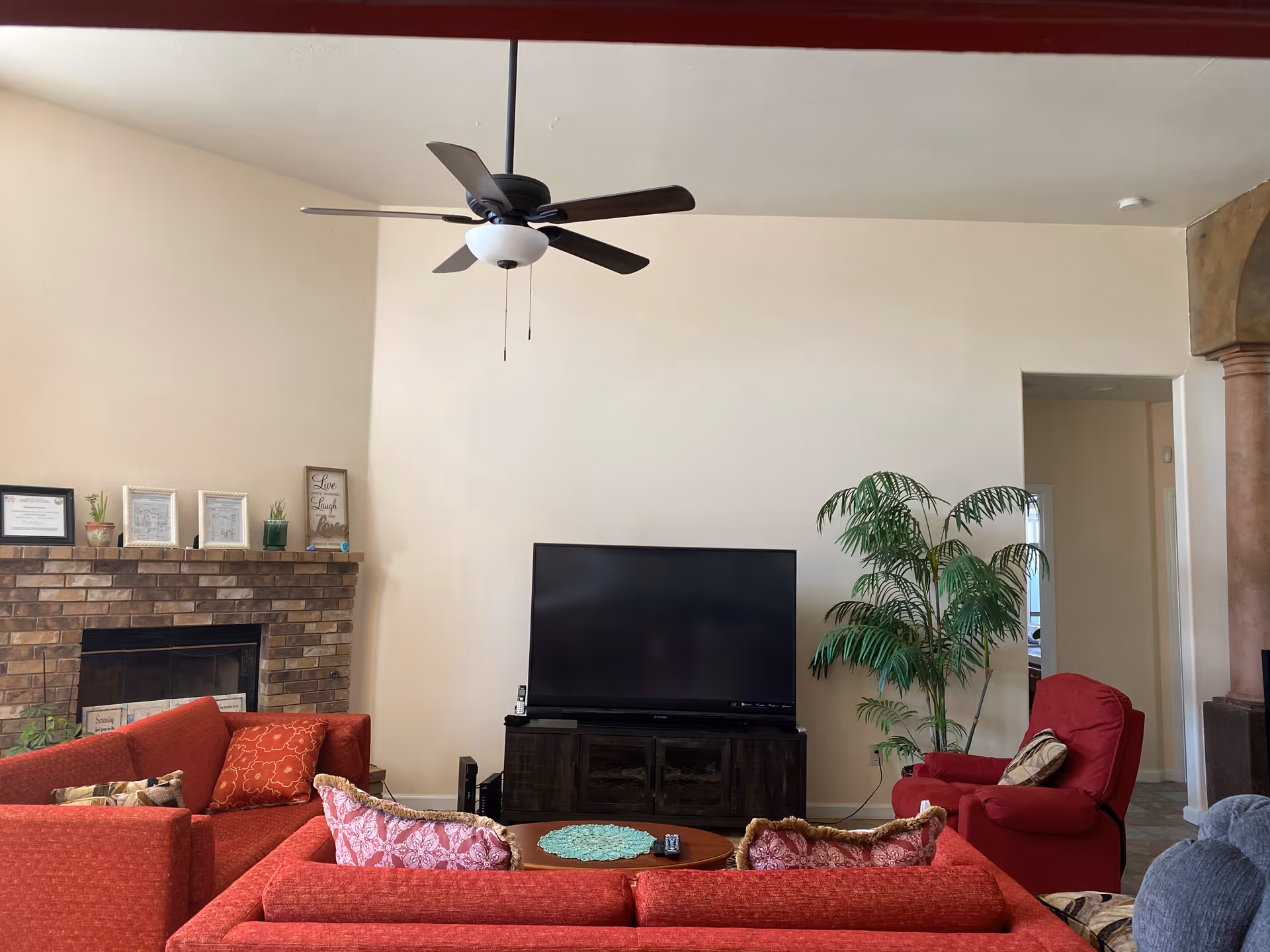 Cozy living room interior with red seating, a fireplace, TV, ceiling fan, and plant.