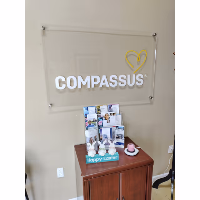 Interior wall with COMPASSUS sign and brochure display on a wooden cabinet.