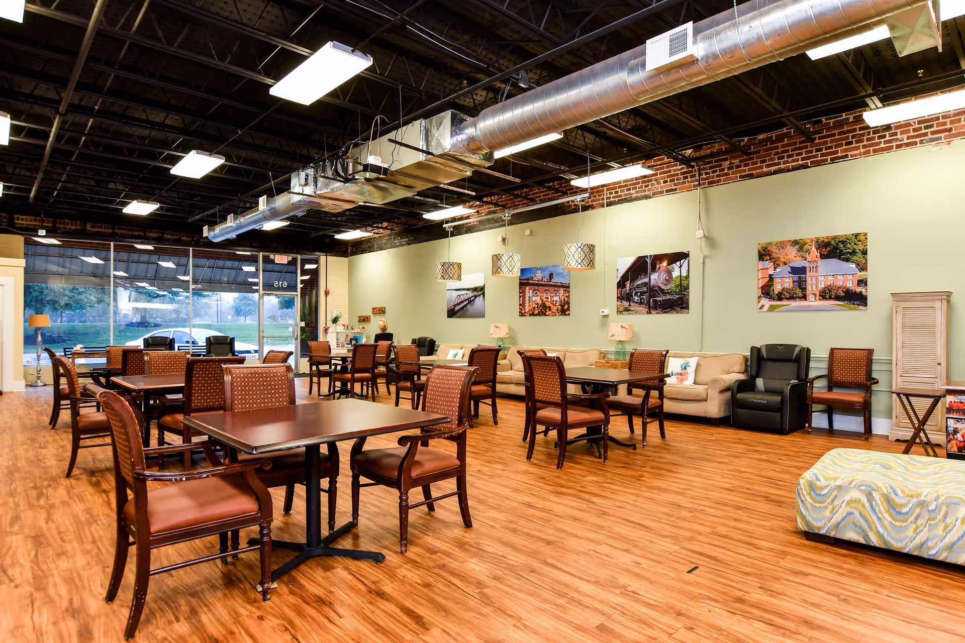 A spacious senior living common area with wooden floors, tables, chairs, and lounge seating.