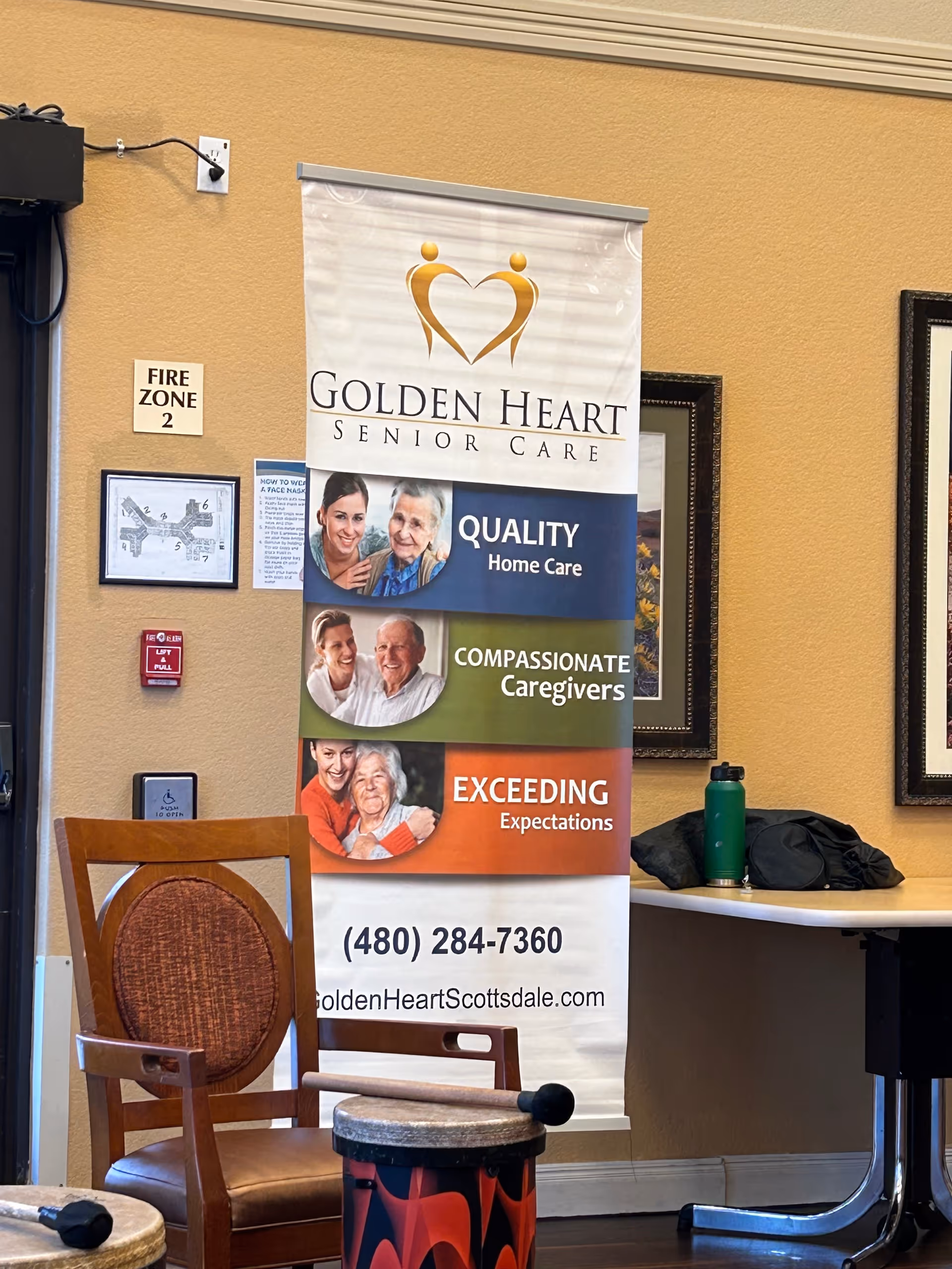 A vertical Golden Heart Senior Care banner stands in a lobby with chairs and a table.