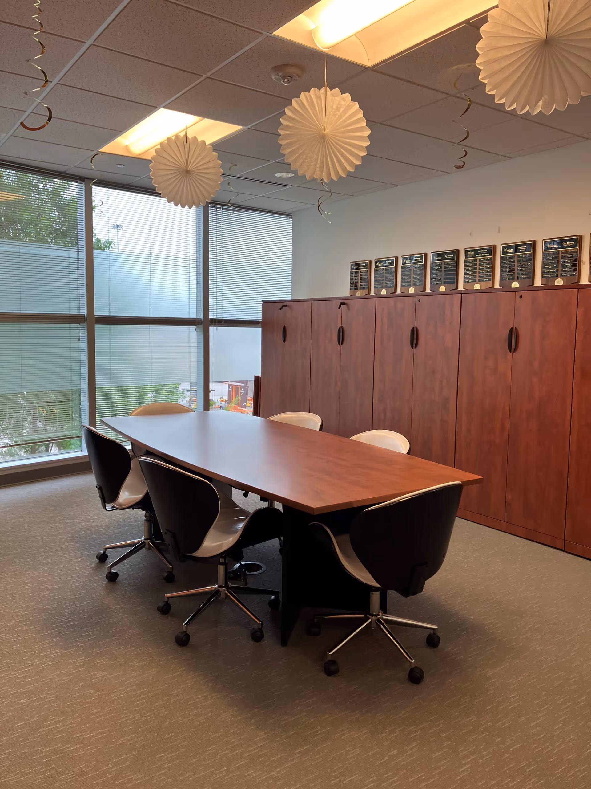 Long wooden table with black-and-white swivel chairs in a bright room with lockers