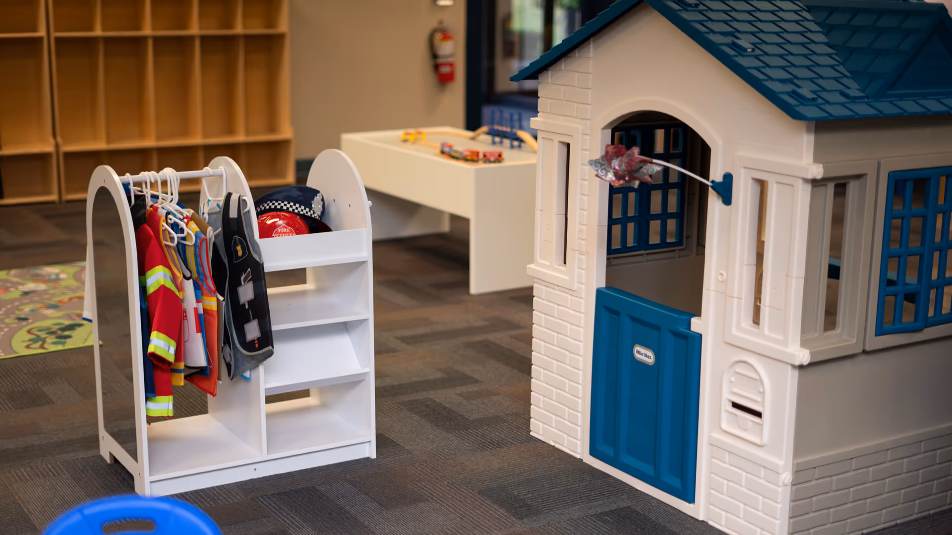 Indoor play area with a plastic toy house and clothing rack.