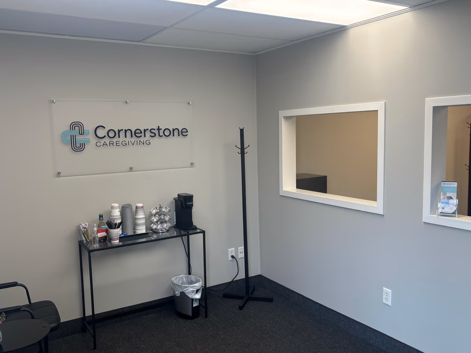 Cornerstone Caregiving sign on wall with beverage station and coat rack.