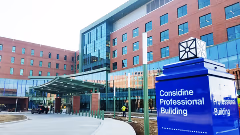 An exterior view of a brick medical building with glass windows and a blue sign.