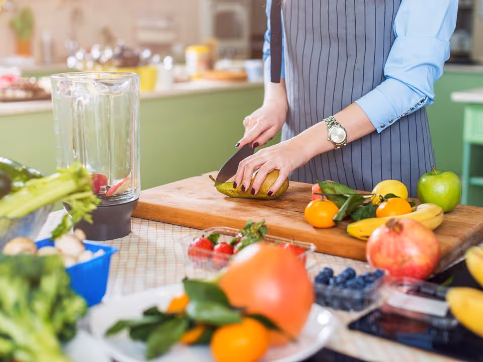 Person chops fruit on a cutting board in a bright kitchen.