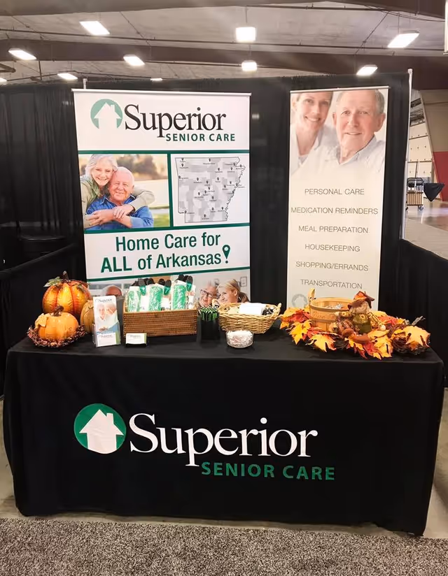 Indoor expo booth displaying Superior Senior Care banners, pumpkins, and fall decor on a black table.