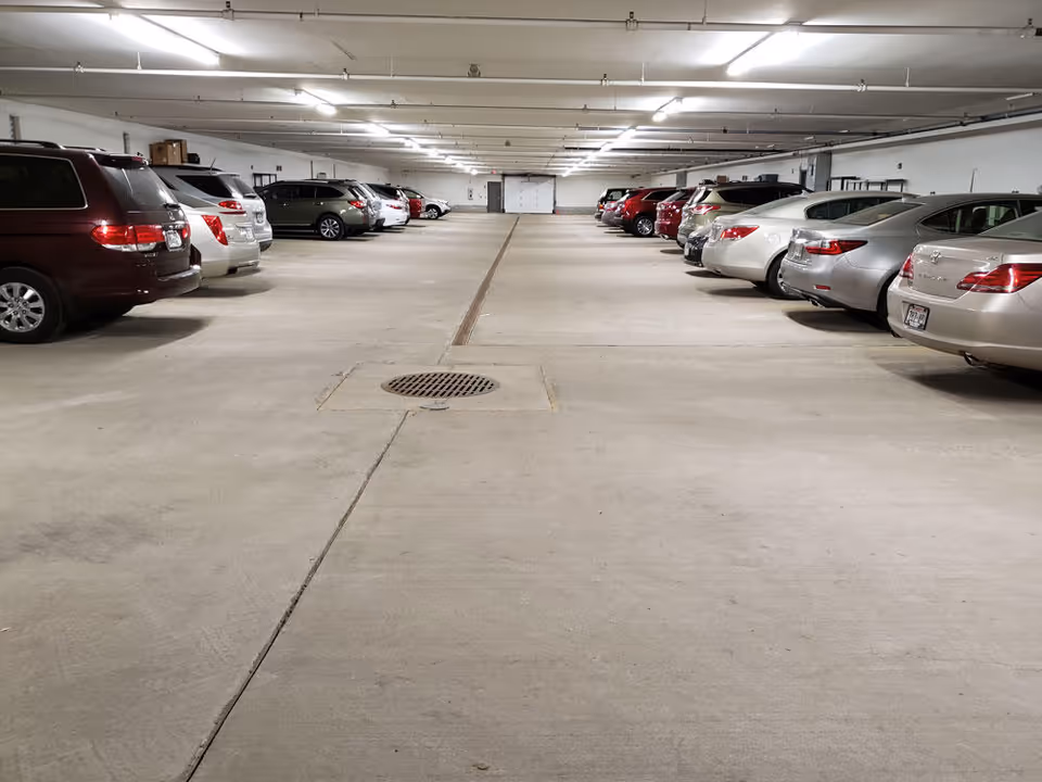 Indoor parking garage with rows of cars on both sides and bright ceiling lights.