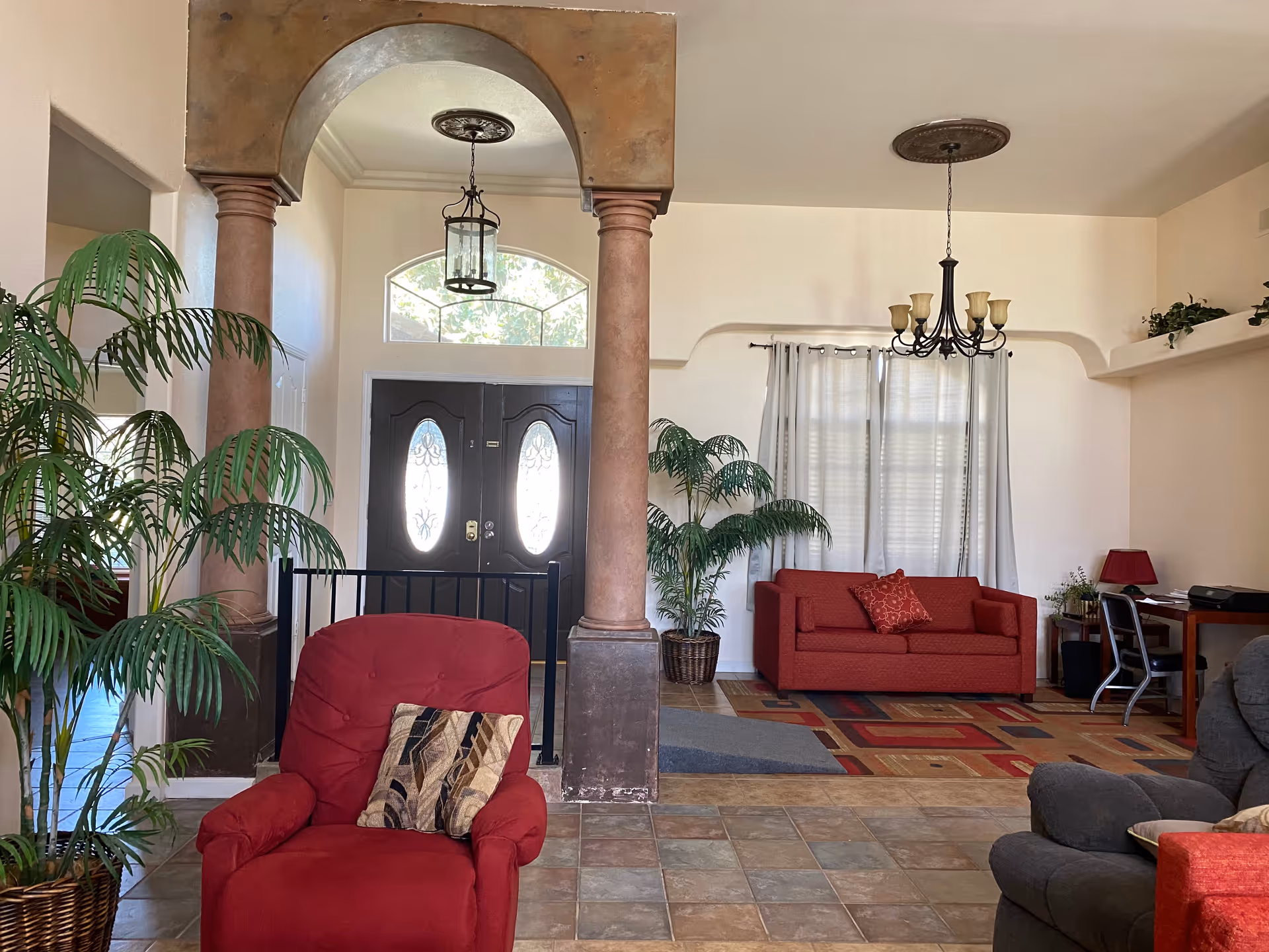 Spacious lobby area with red seating, plants, archways, and a front door.