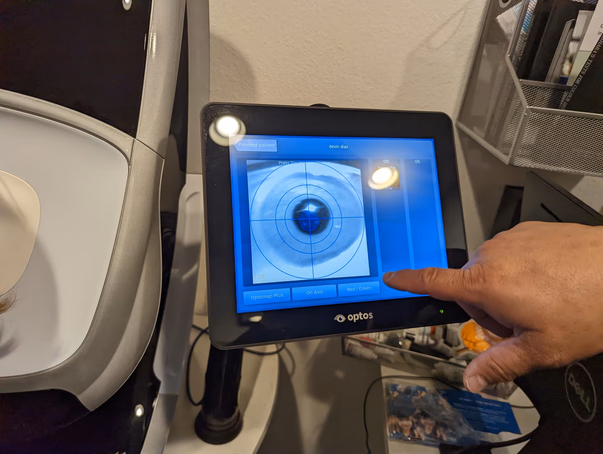 Close up of a hand operating an Optos eye imaging touchscreen in a clinic.
