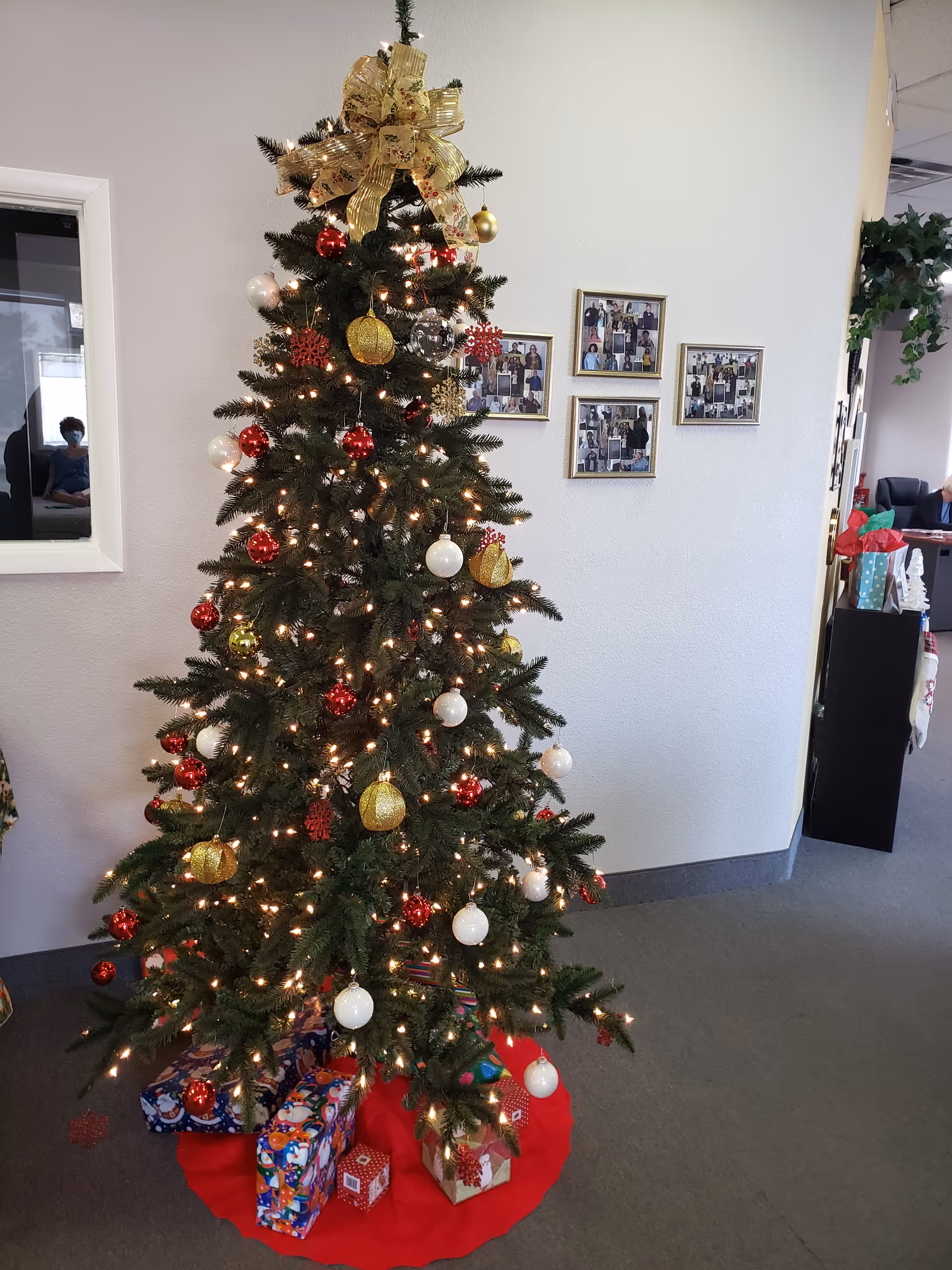 Decorated Christmas tree with wrapped gifts in a lobby hallway at Comfort Keepers Home Care.