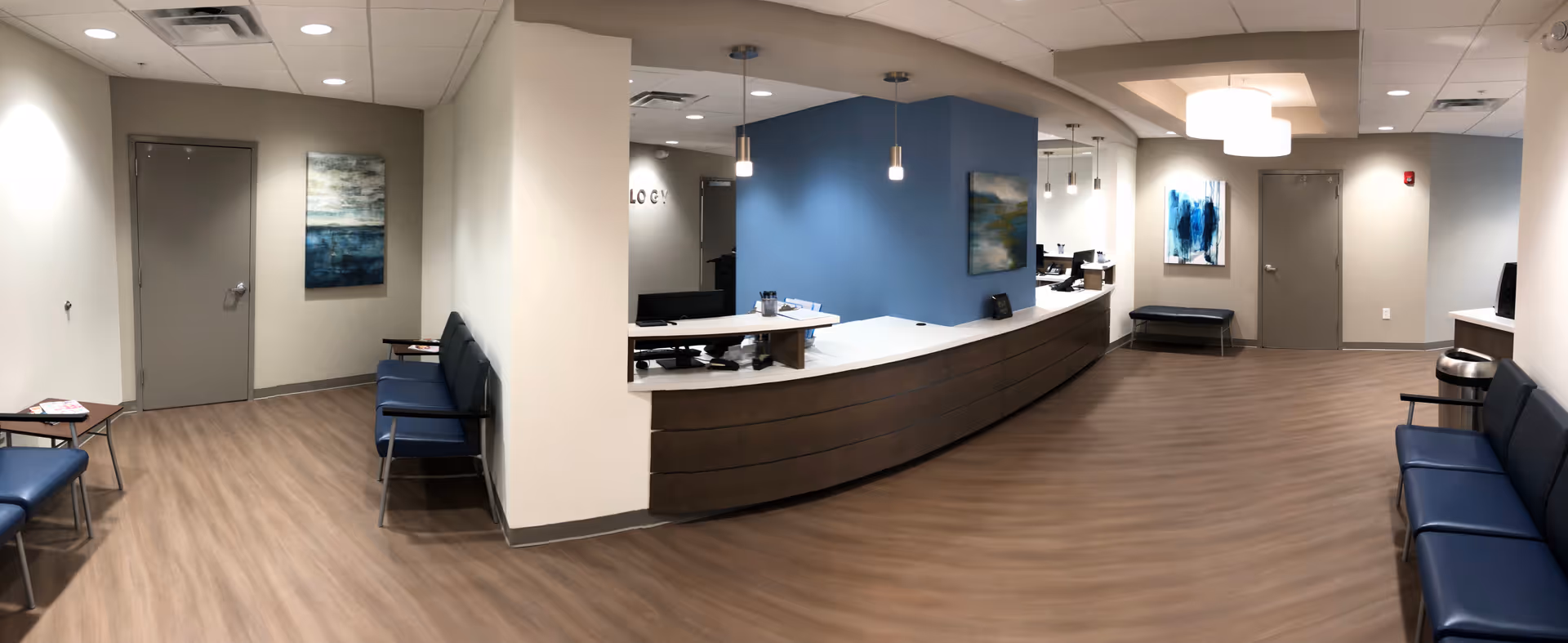 Wide view of a curved reception desk, blue wall, and seating in a clinic lobby.