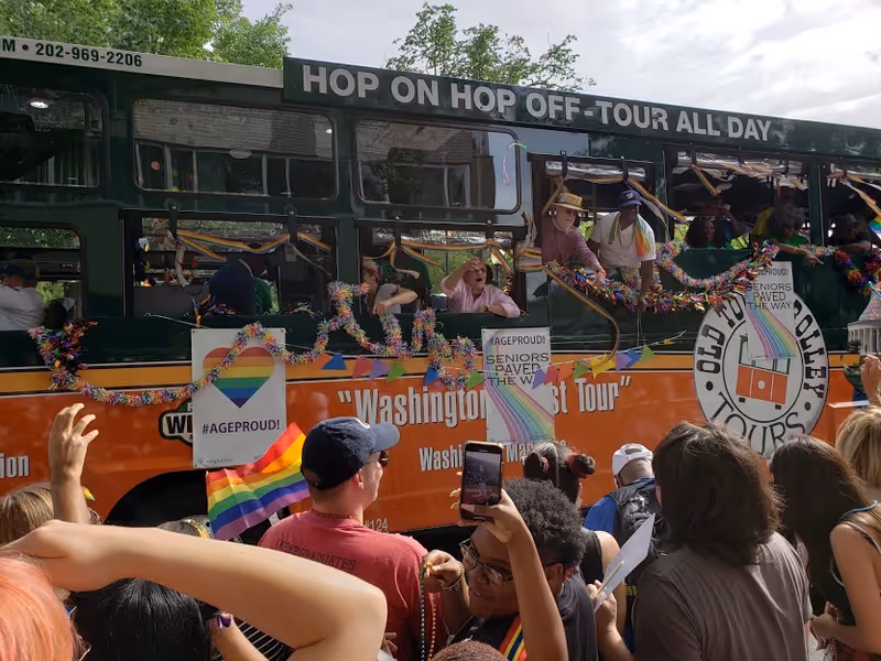 Crowd gathers beside a colorful tour bus in a lively outdoor parade.