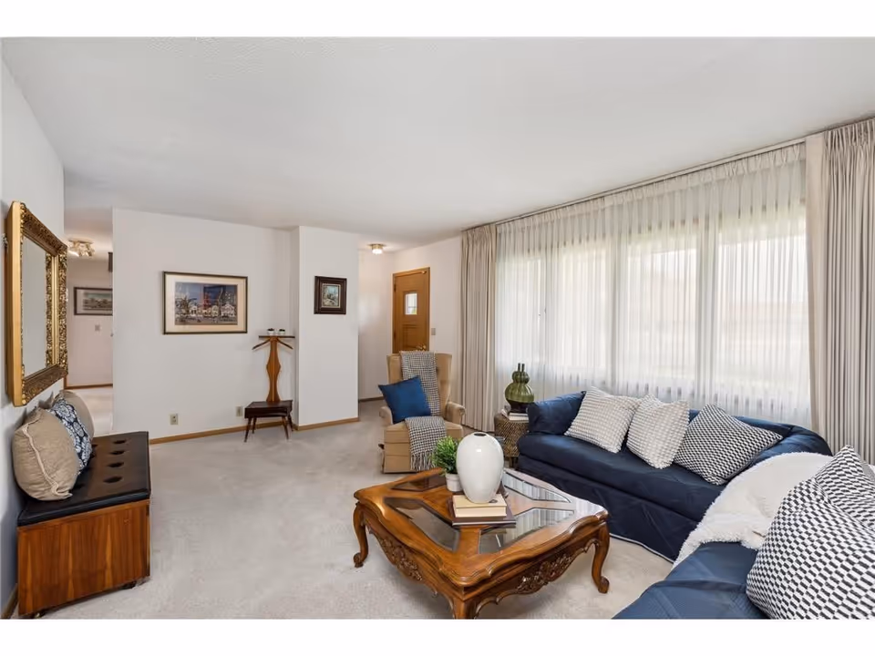 Bright living room with navy sofas, glass coffee table, and large sheer-curtained windows.