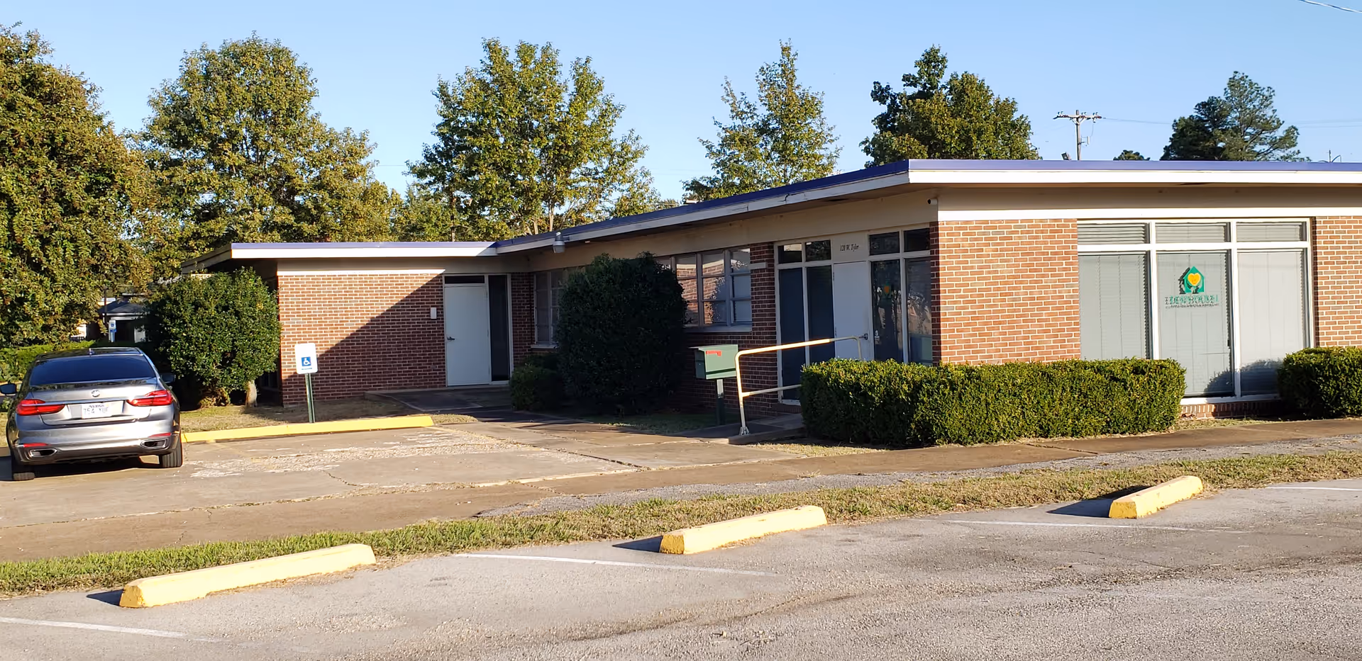 A single-story brick building with large windows and a small parking lot in front.