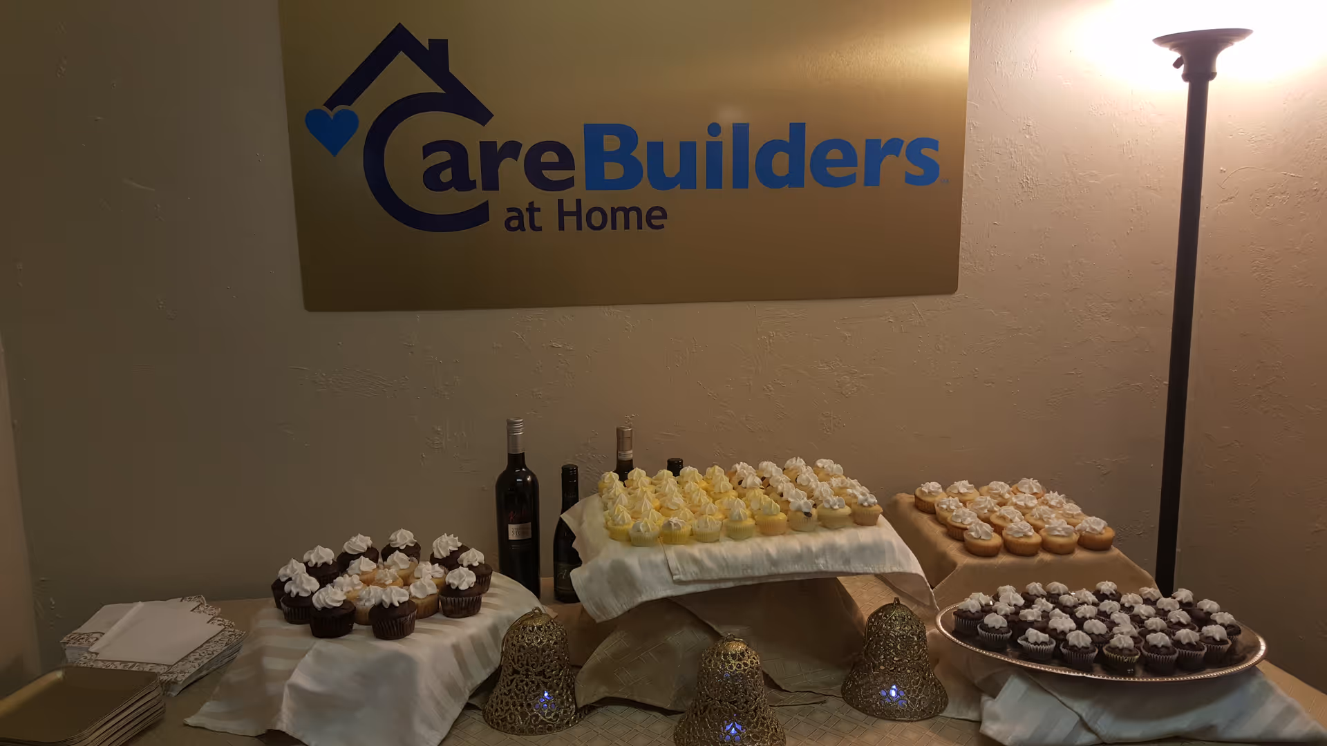 Dessert tables with cupcakes and wine displayed beneath a CareBuilders at Home sign.