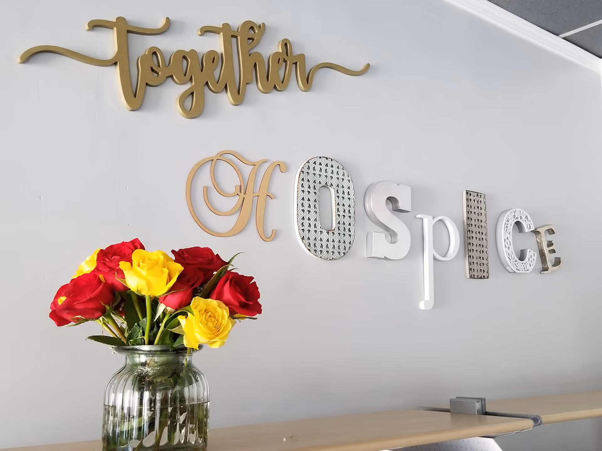 Gold scripted 'Together' sign and 'Hospice' decor with a vase of roses on a counter.