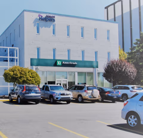 Front exterior of a Senior Helpers building with a parking lot and cars.