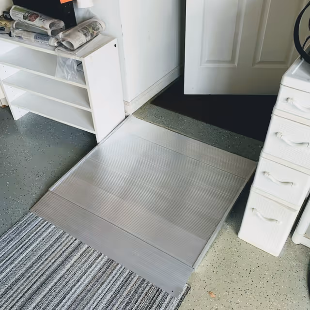 Indoor view of a metal wheelchair ramp beside a doorway and nearby shelves.