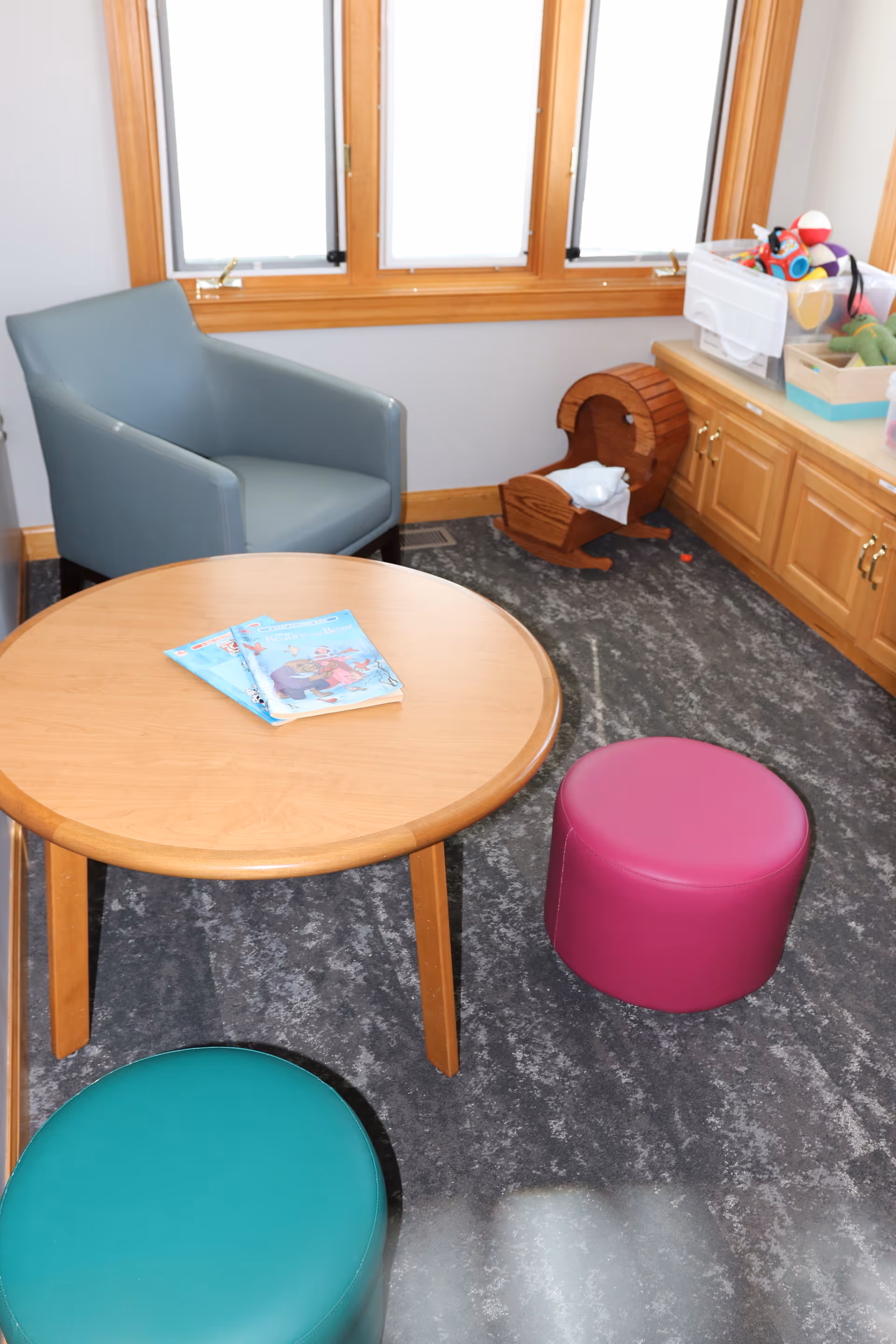 Small kid-friendly lounge in a hospice facility with table, colorful stools, toys.