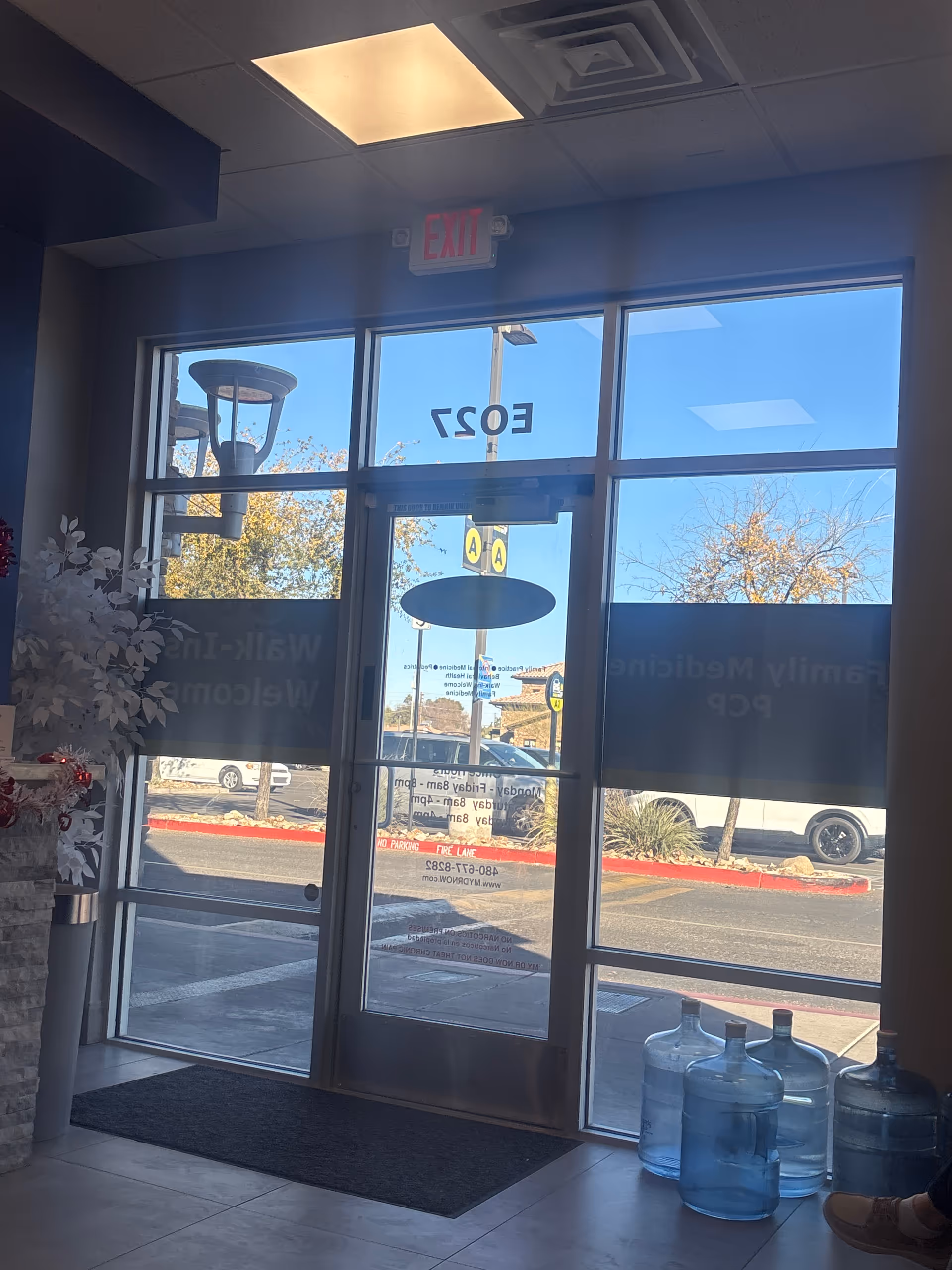 Interior lobby with glass front doors, EXIT sign, and water jugs by the entrance.