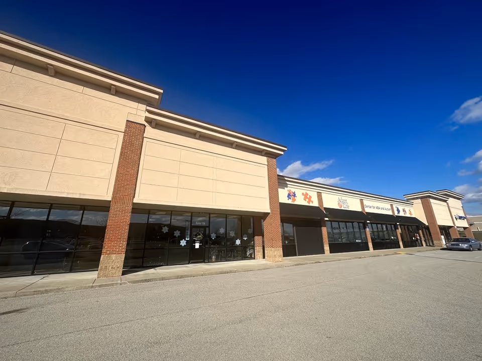 Exterior view of a beige-brick storefront complex with large windows and blue sky.