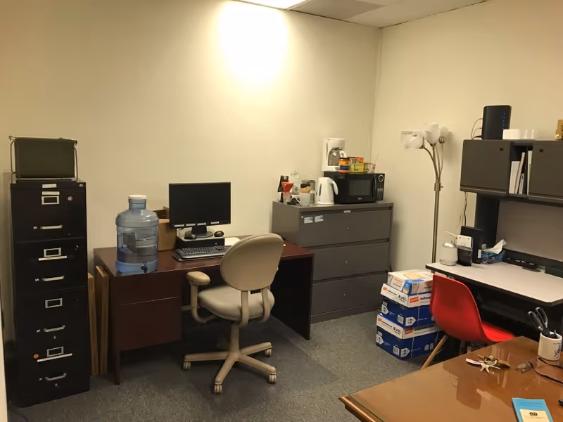 Interior staff office with desk, computer, filing cabinets, water cooler, and supplies.