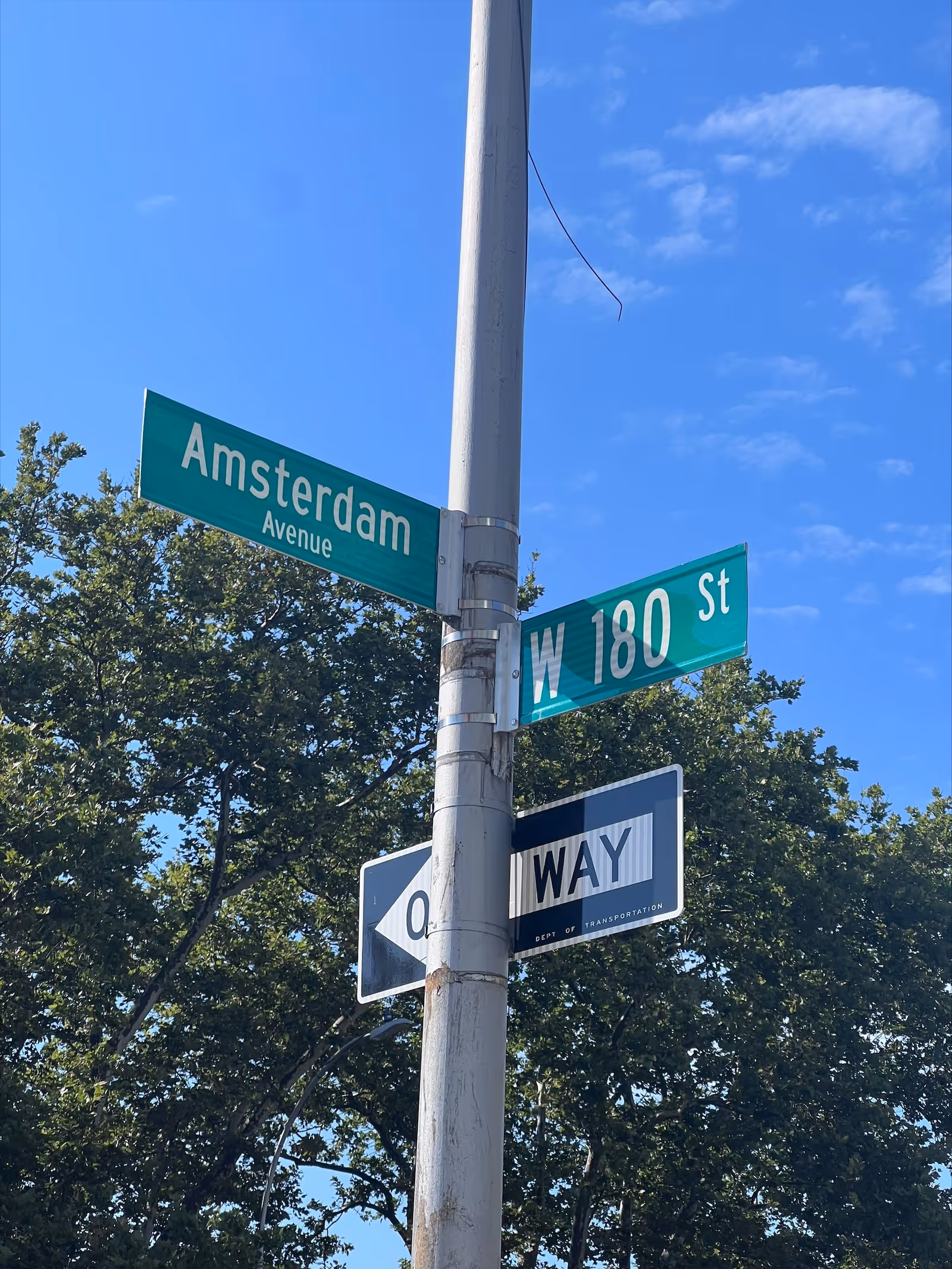 Street corner with Amsterdam Avenue and West 180th Street signs against blue sky.