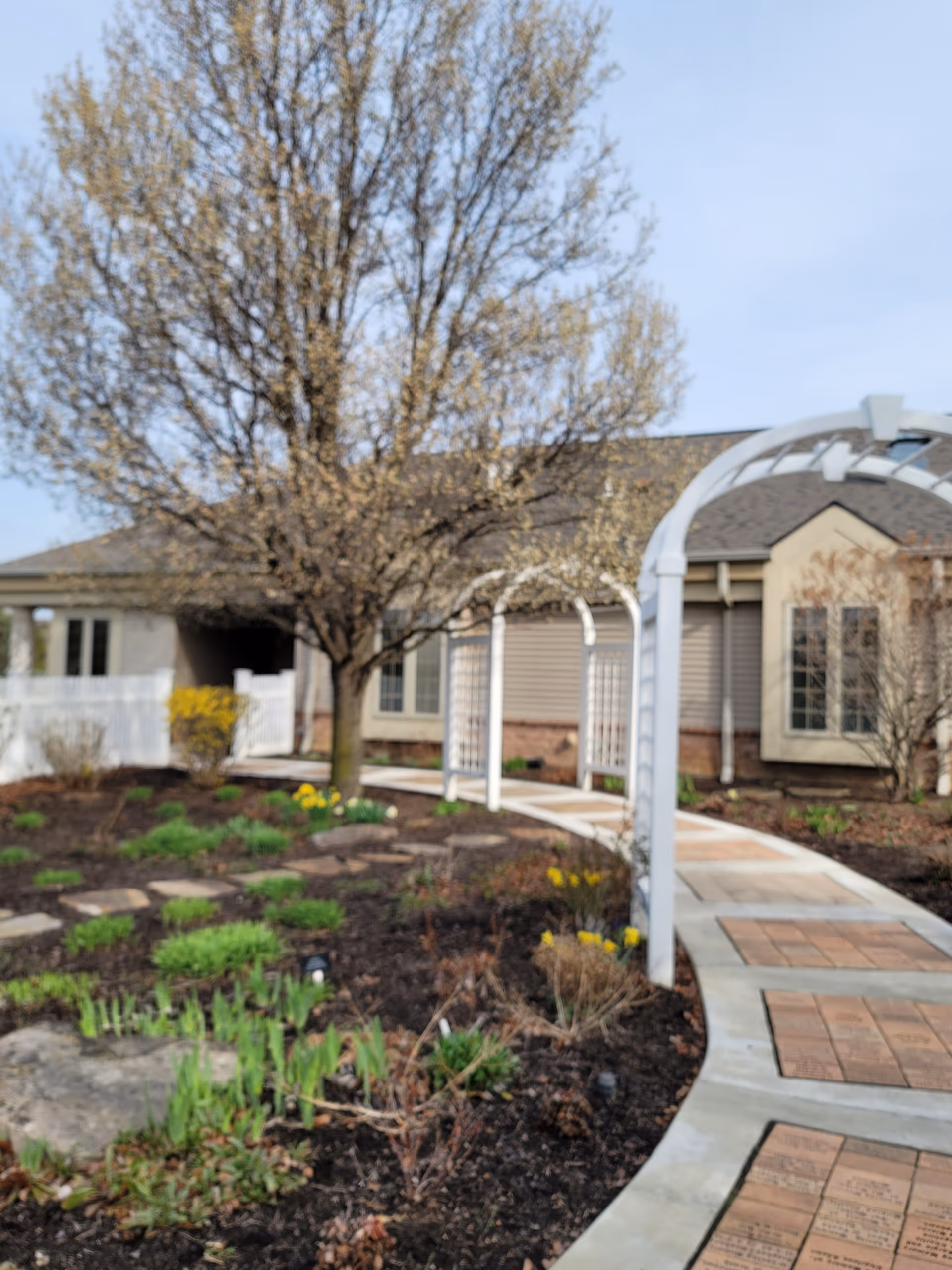 Pathway and landscaped garden lead to a facility entrance under an arched pergola