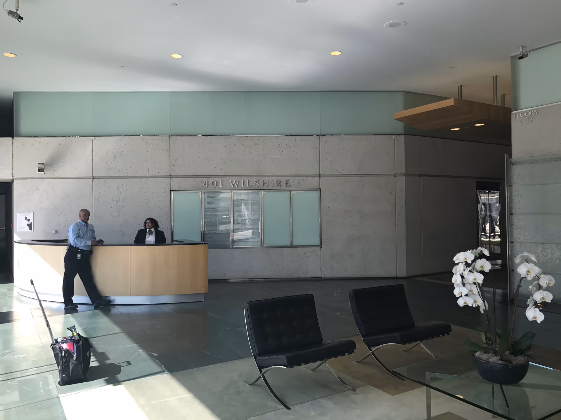 Lobby reception area with two staff members behind a curved beige desk.