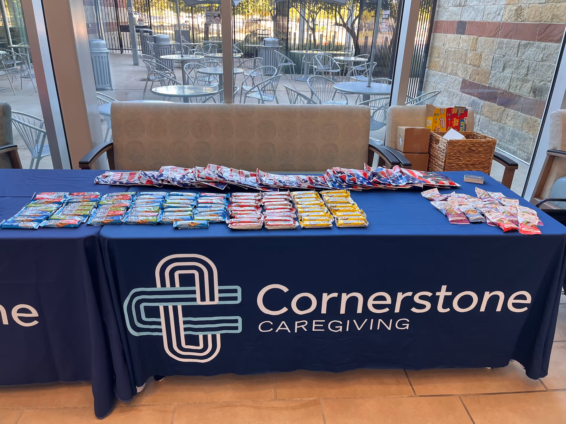 A long table covered with a blue cloth displays snacks and Cornerstone Caregiving branding.