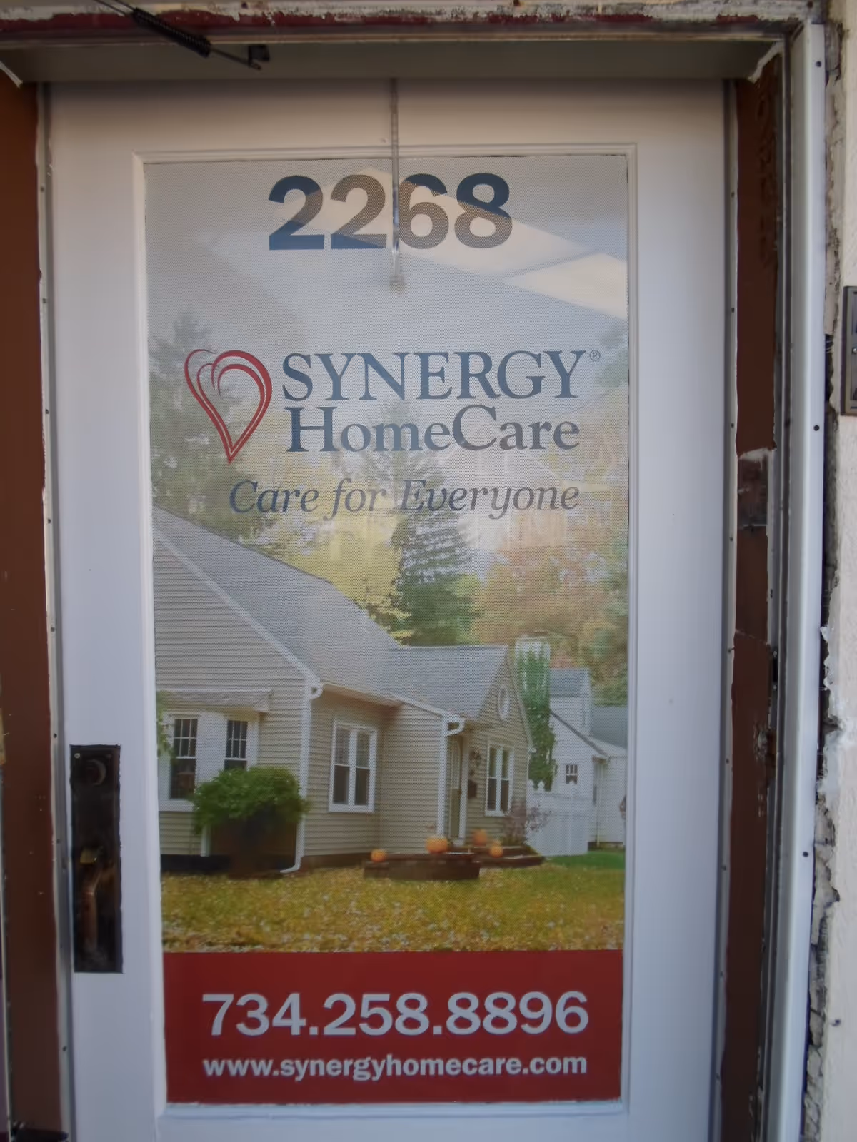 Front door of a Synergy HomeCare building displaying logo, address numbers, and contact info.