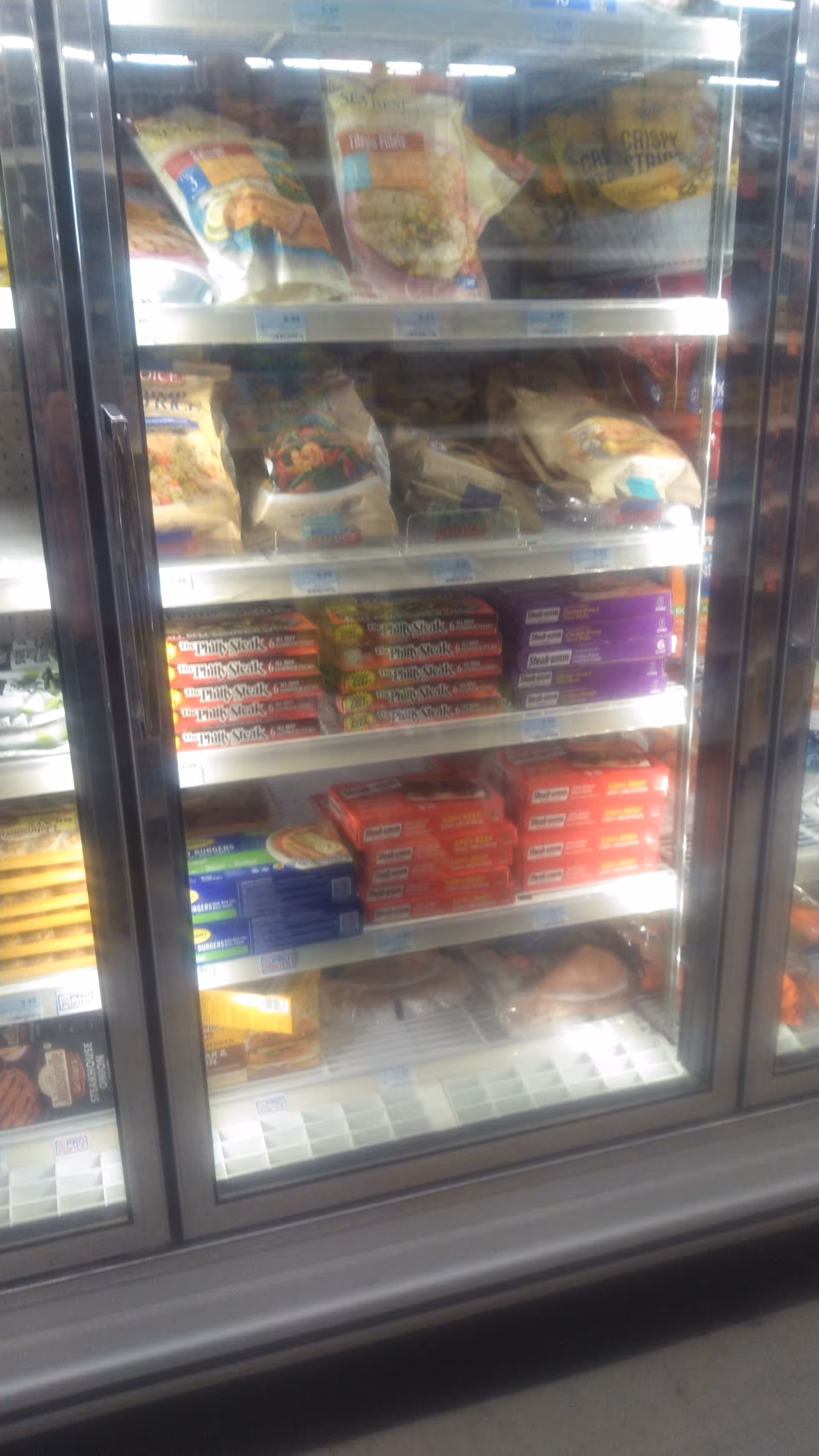Glass-front refrigerated display stocked with frozen meals and snacks inside.