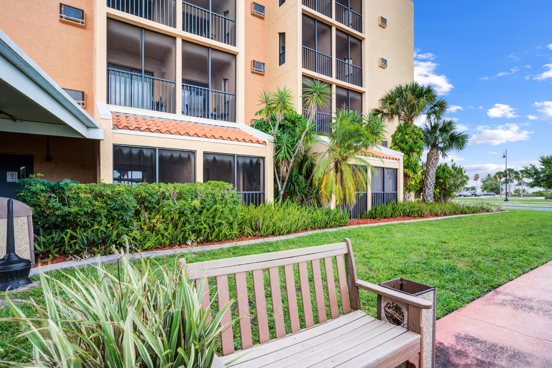 Outdoor view of a senior living building with a bench and manicured landscaping.