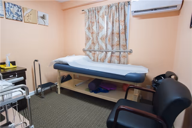 Physical therapy treatment bed in a peach-colored exam room with curtains and equipment.