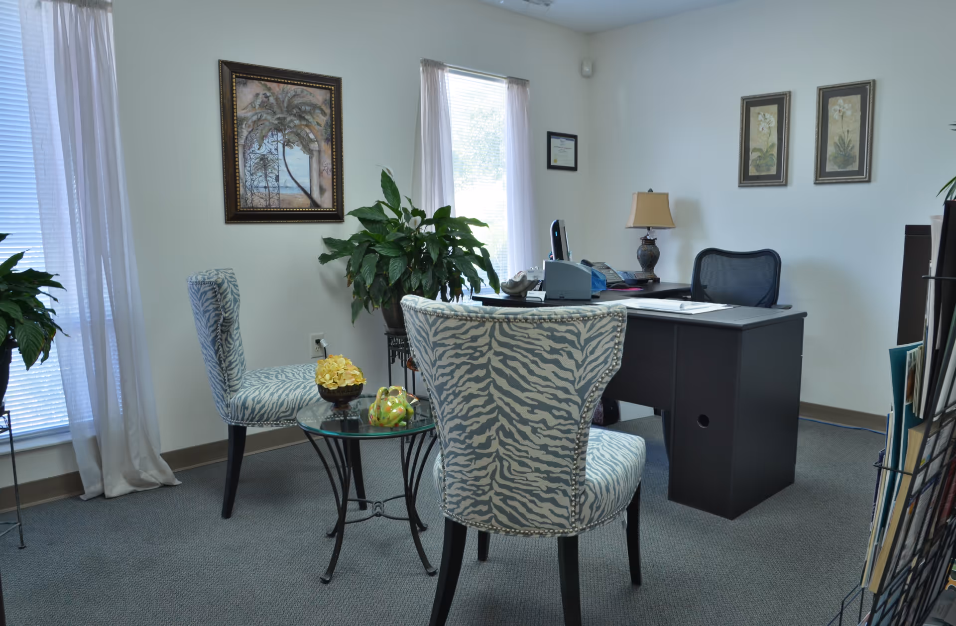 Office reception area with a desk, zebra-patterned chairs, plants, and framed art on the walls.