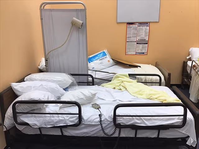 Two hospital beds with rails, a monitor, and a yellow blanket in a patient room.