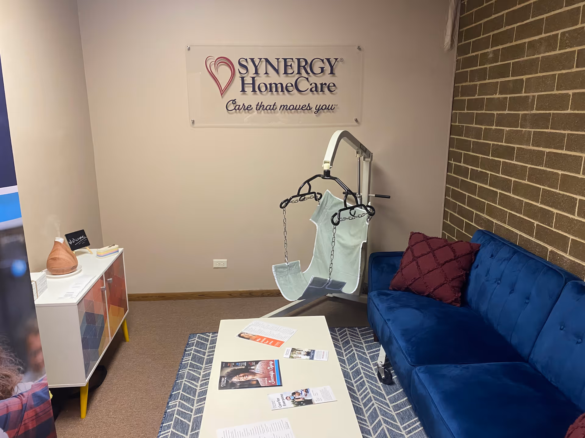 Small interior lounge with blue sofa, hanging chair, and SYNERGY HomeCare sign.