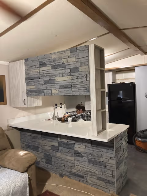 In an indoor kitchen with stone-faced island, a person works at the counter.