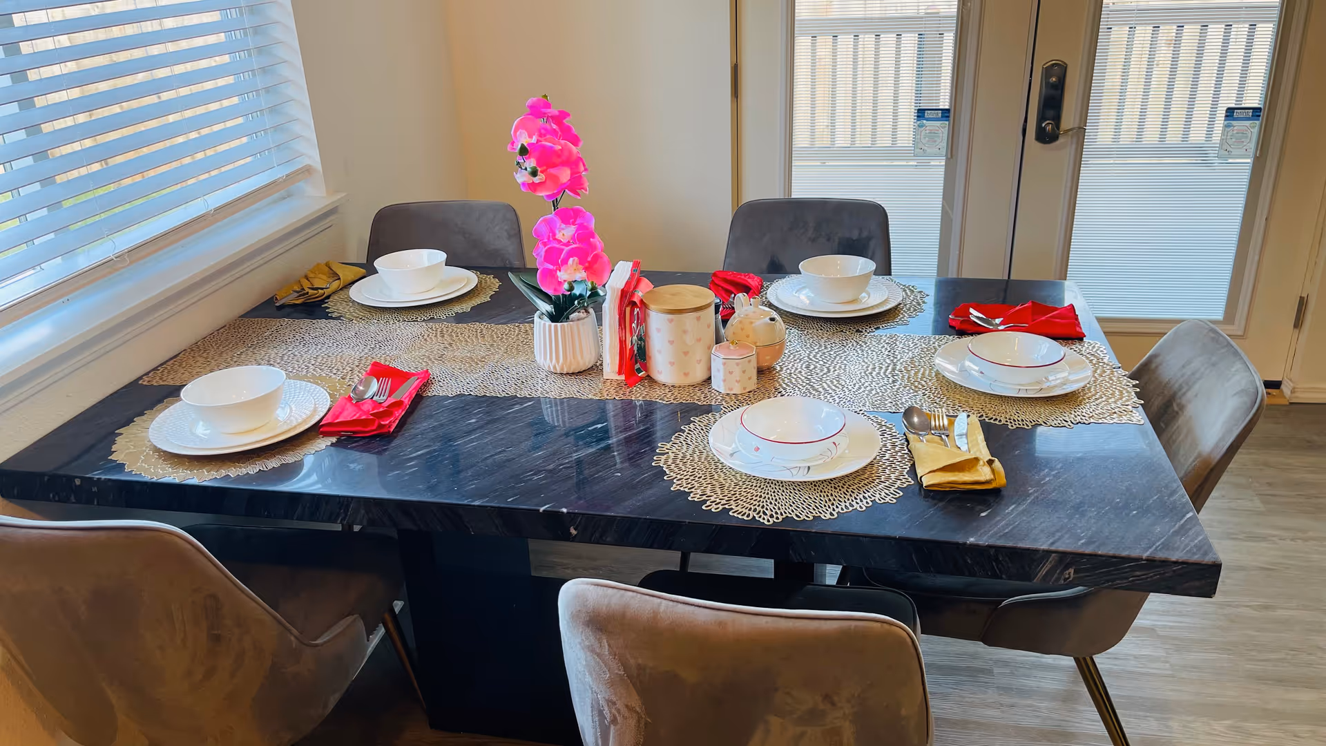 Dining table set for six with dishes, napkins, and pink orchid centerpiece.