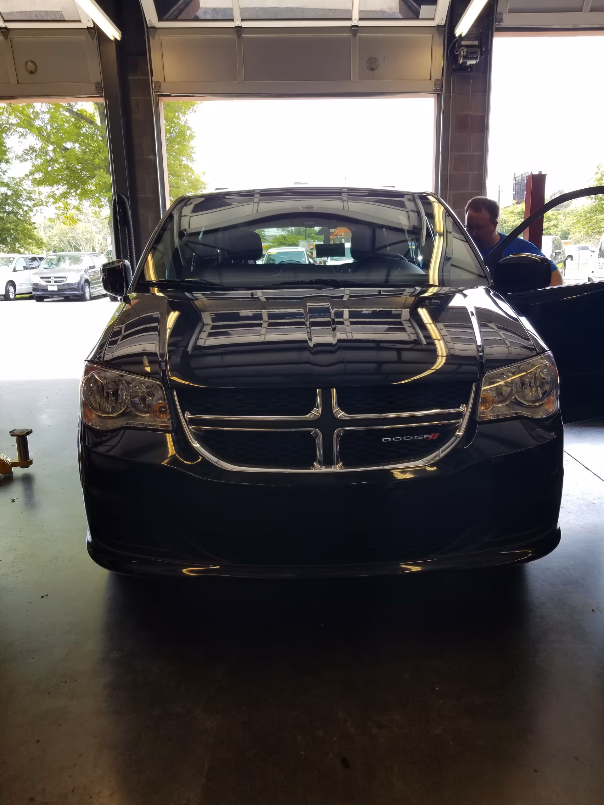 A black Dodge SUV sits in a service bay with a technician nearby.