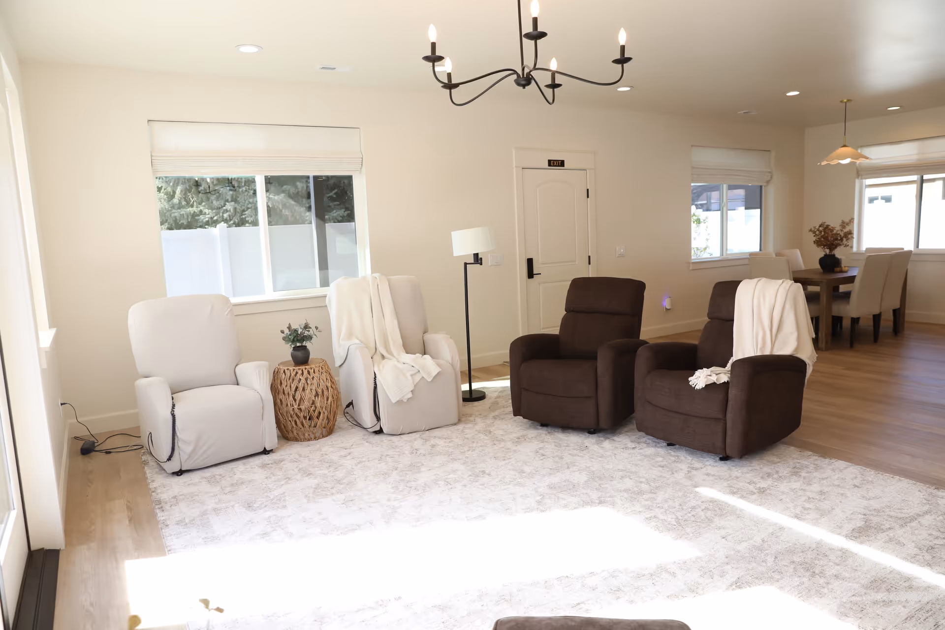 Bright common living room with recliners, a rug, and a dining area in the background.
