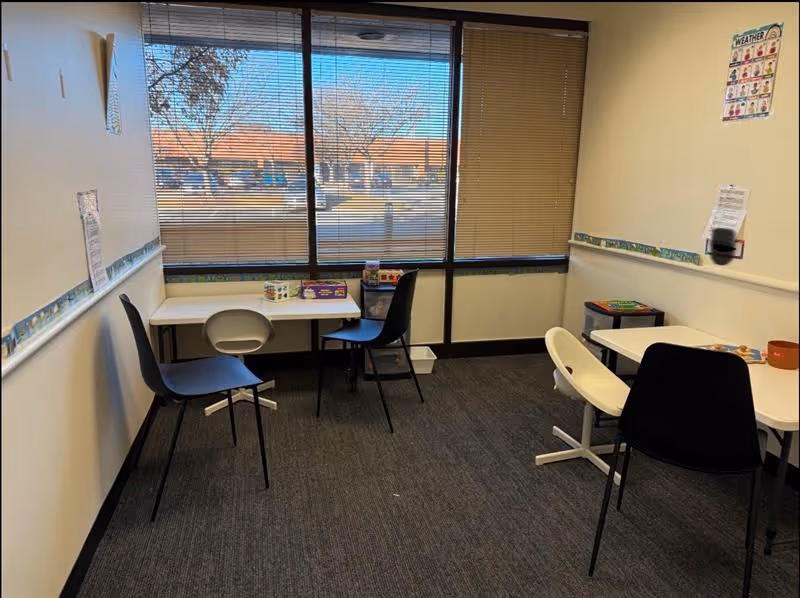 Small interior activity room with tables and chairs beside a large window.