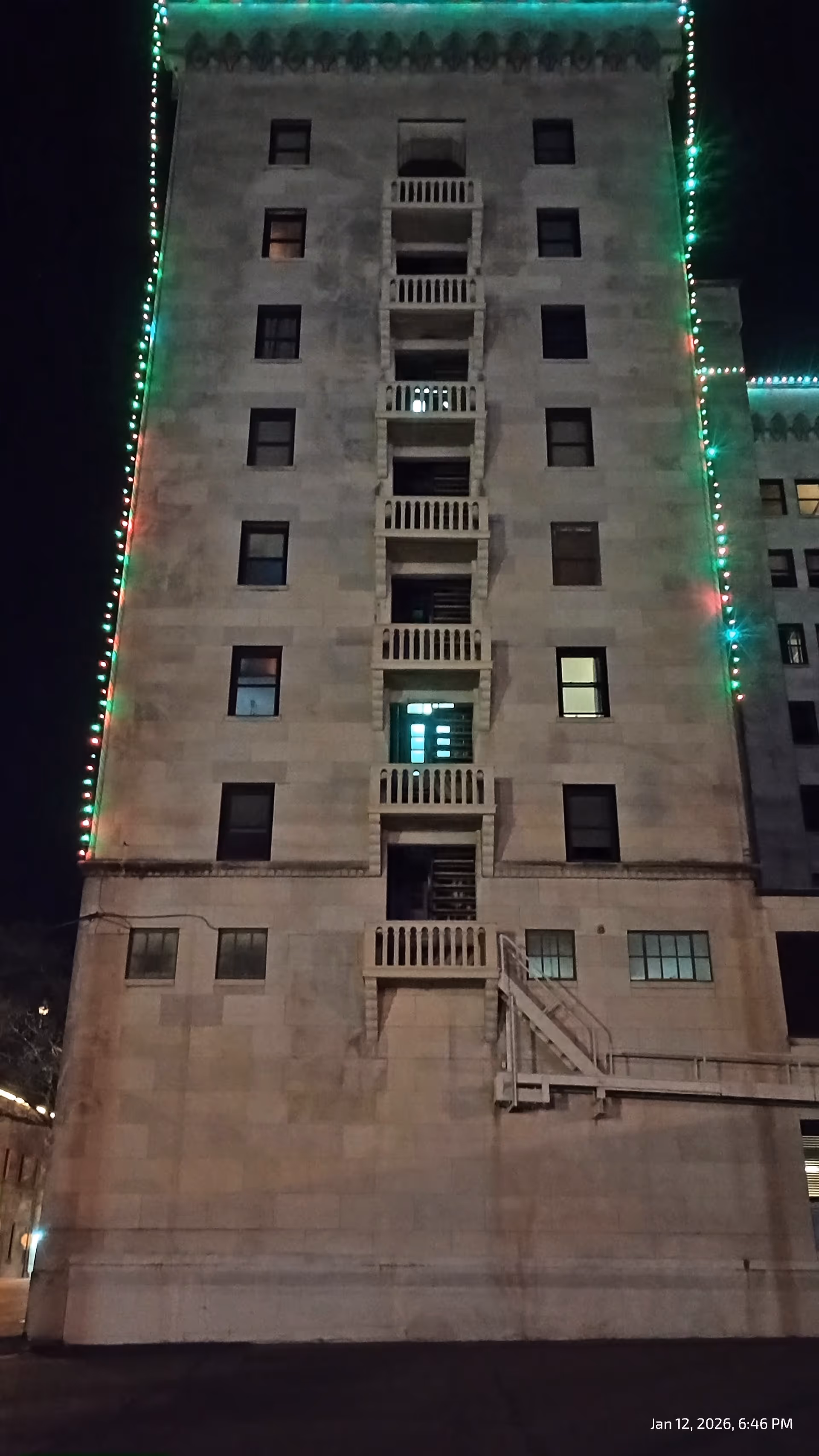 Tall beige building at night with an external stairway and colorful lights along edges.
